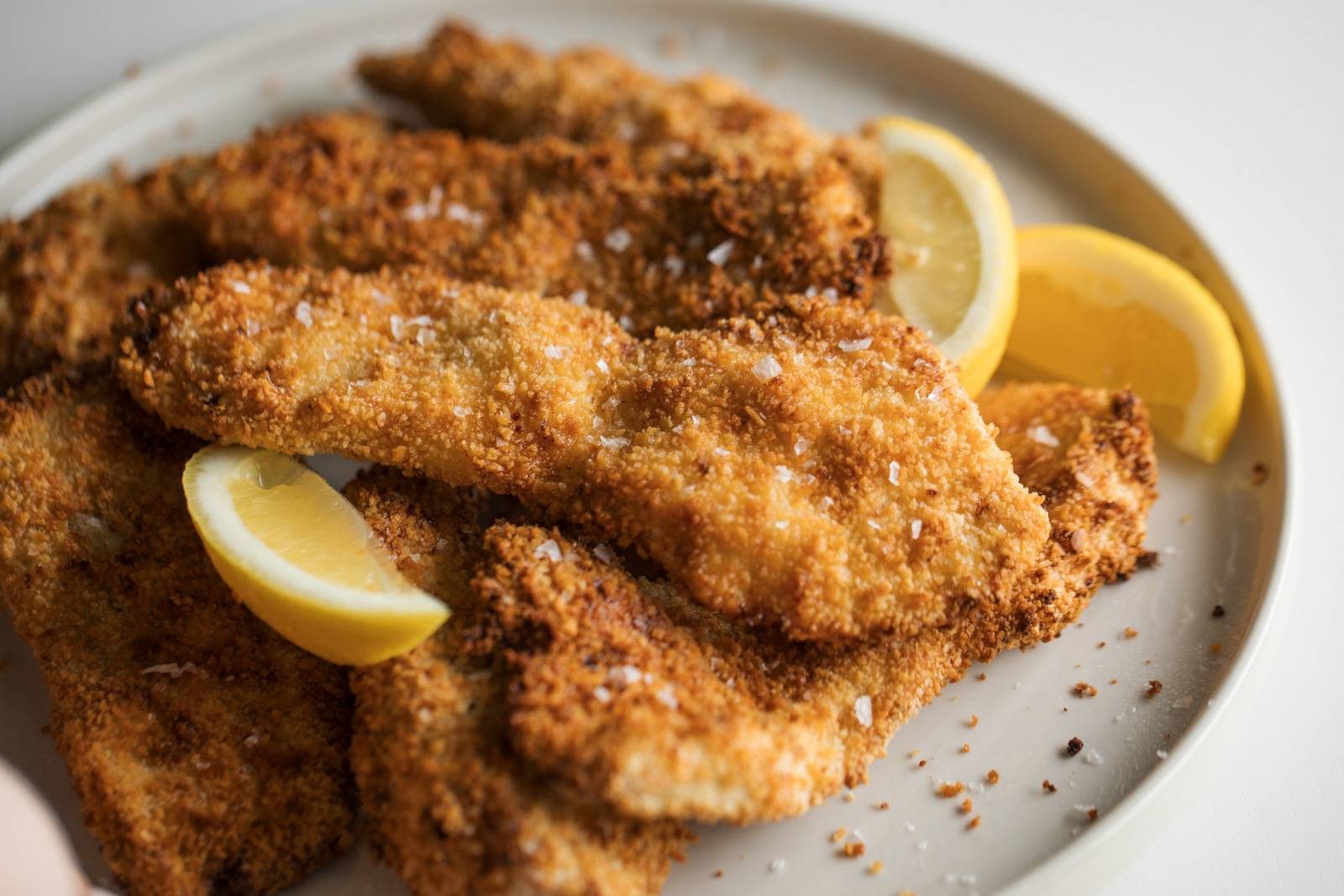 Crispy chicken cutlets on a plate with lemon wedges.