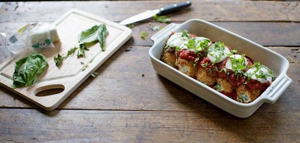Basil on cutting board next to chicken rolls in a white baking dish.
