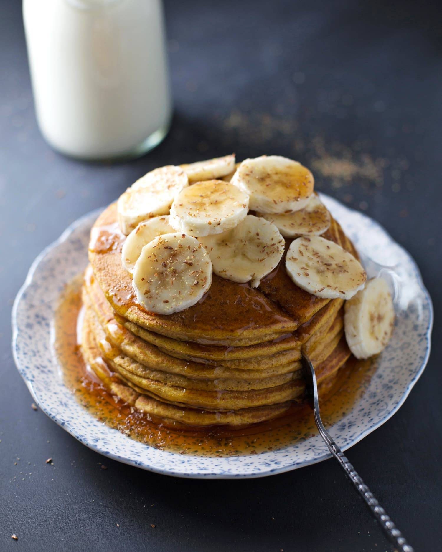 Whole wheat pumpkin pancakes stacked on a plate with bananas.