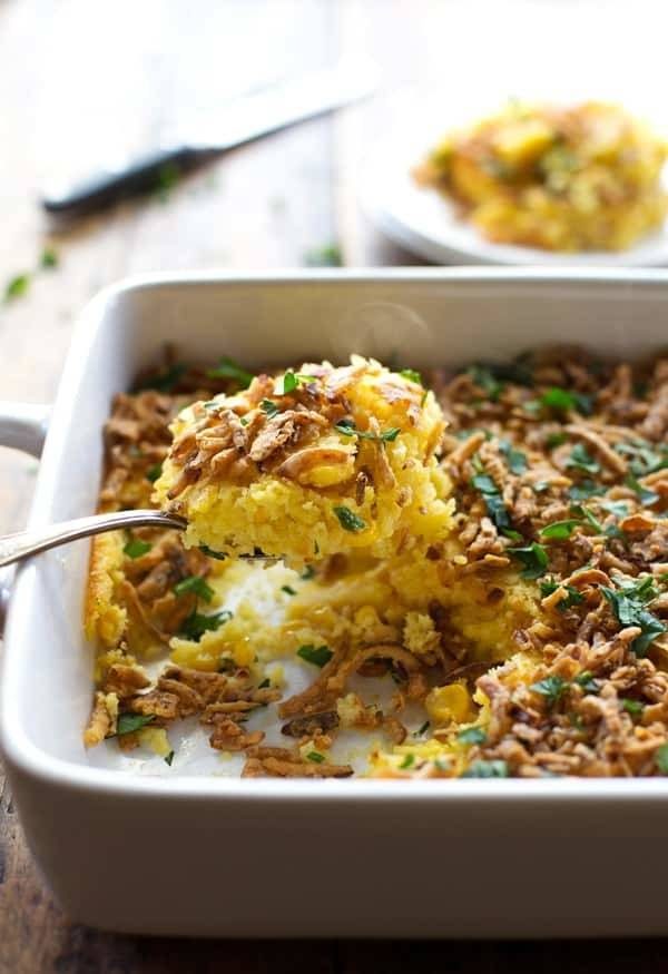Corn pudding with crispy onions and herbs on a spoon and in a baking dish.
