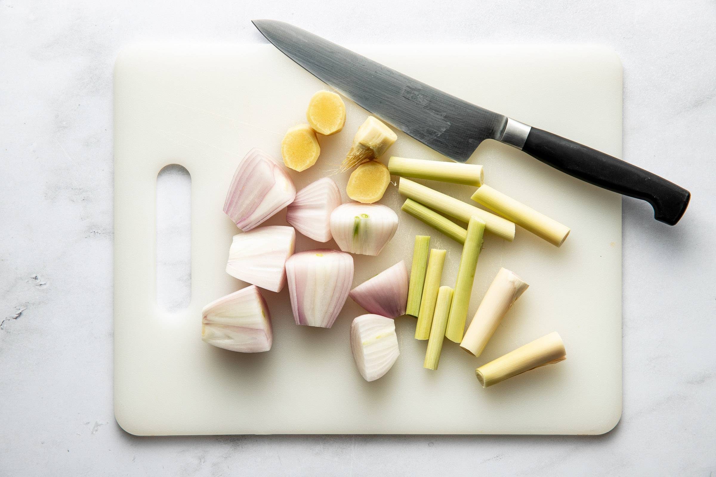 Shallots, lemongrass, and ginger on a cutting board.