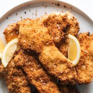 Crispy chicken cutlets on a plate with lemon wedges.