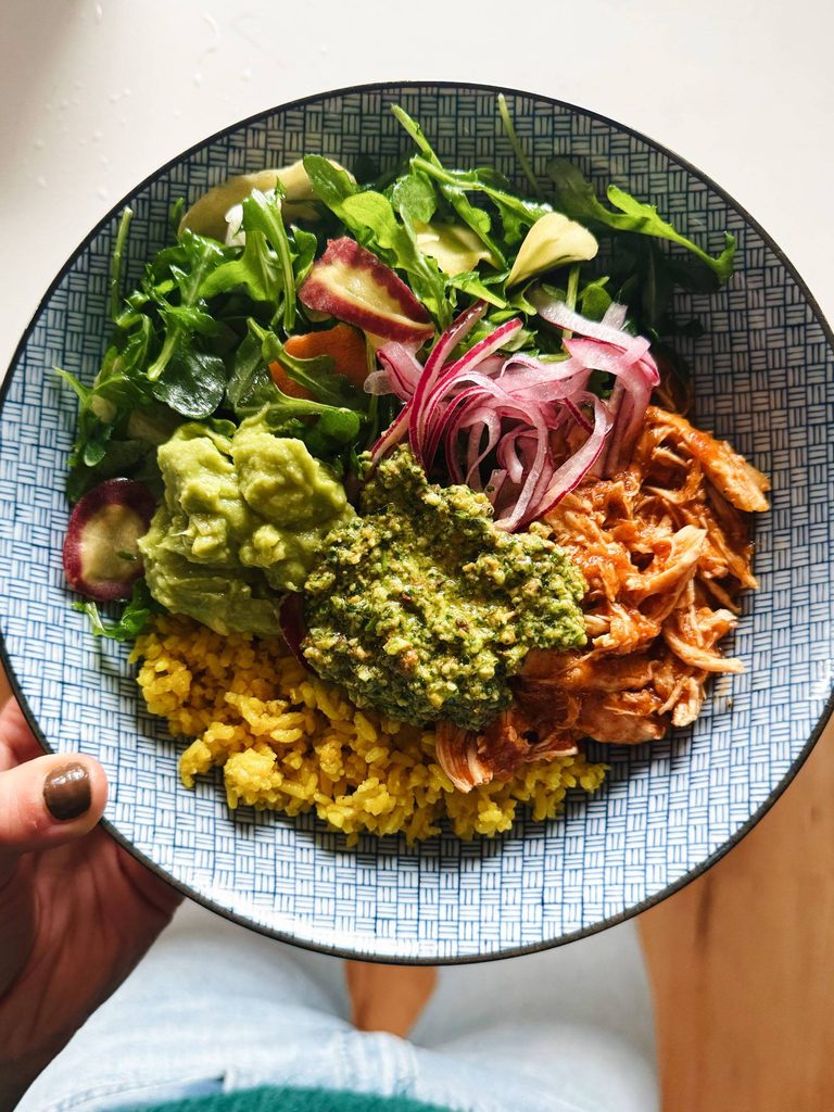 Shredded chicken in a bowl with rice, greens, onions, and cilantro pesto.
