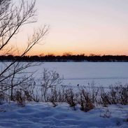 A winter scene with snow covering an empty field beneath a sky tinged with orange.