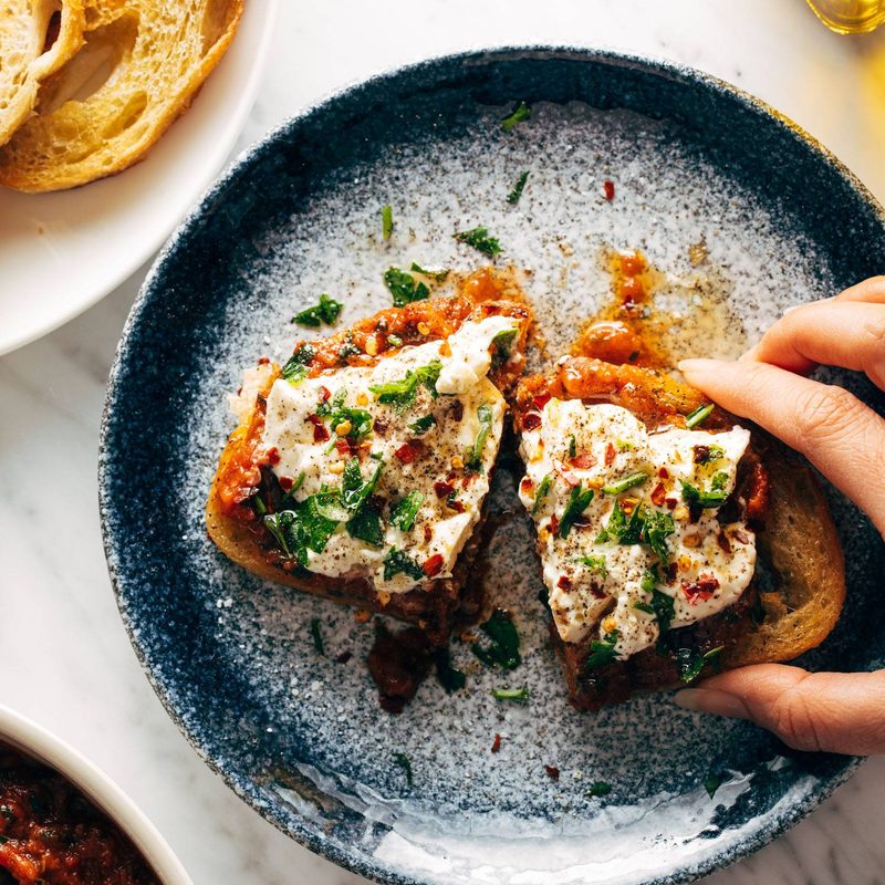 White hand grabbing Zaalouk toast on a plate